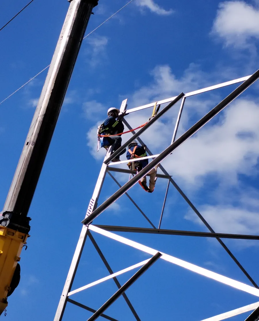 Montaje de torre de telecomunicaciones con grúa y personal asegurado en altura